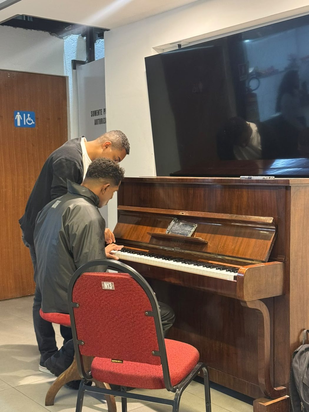 Aluno tocando piano com o professor acompanhando de perto