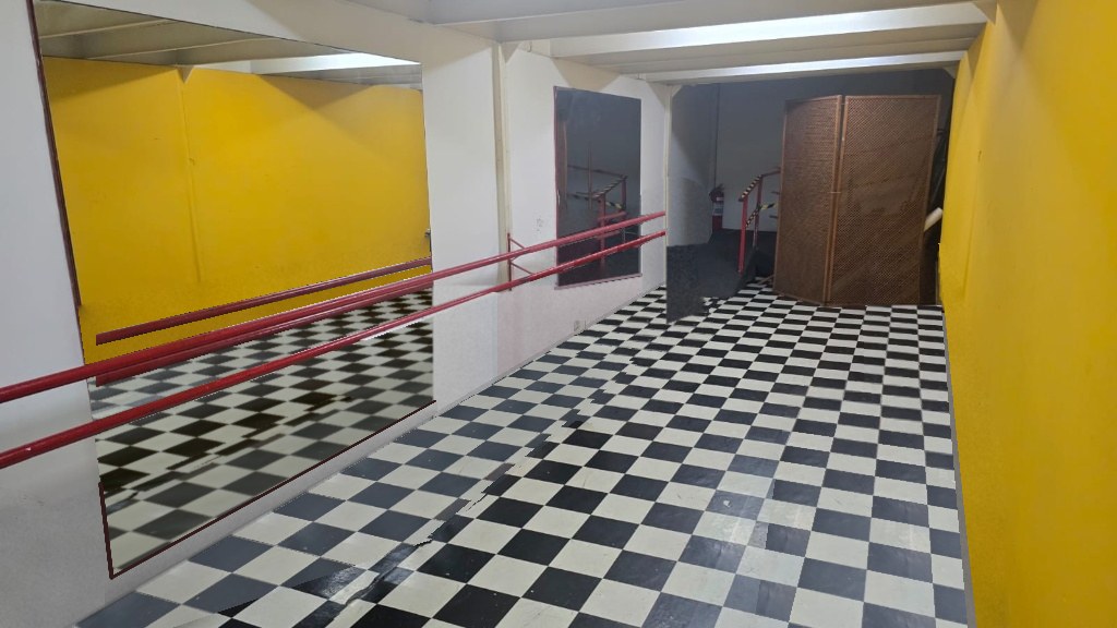 Sala de ensaio do Espaço Cultural Panorama, com espelho e barras vermelhas, paredes amarelas e piso xadrez preto e branco